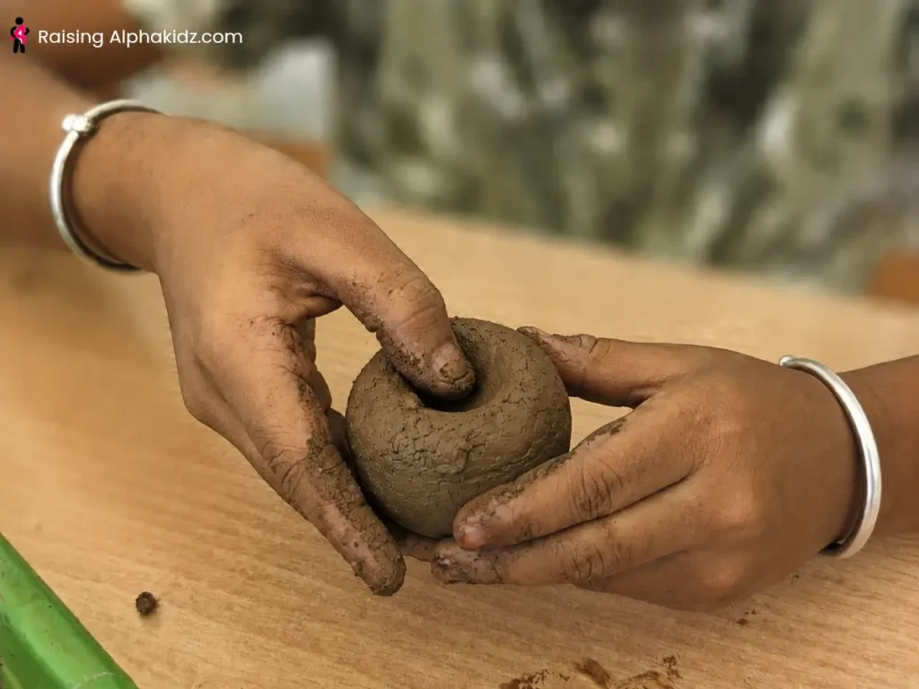 Child pressing a thumb into clay ball to start a pinch pot
