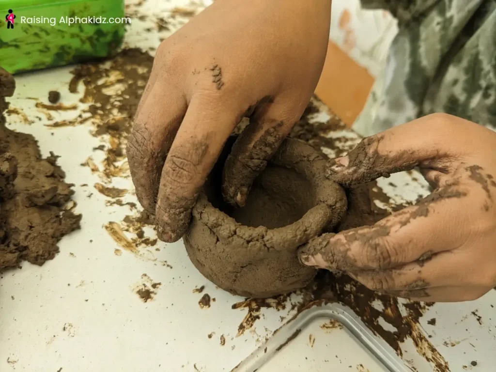 Hands pinching and shaping clay walls to form a pinch pot